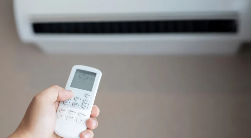Pessoa ajustando o controle remoto de ar condicionado com o termômetro na tela mostrando 25°C, ambiente interno confortável.